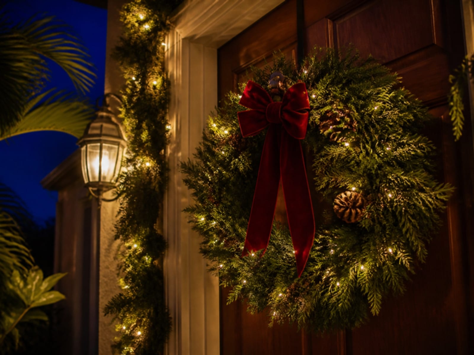 Concept: a fresh wreath with a red bow and warm lights on a dark front door